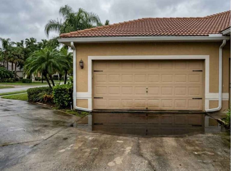 Residential driveway sloping down toward a garage with pooled rainwater.