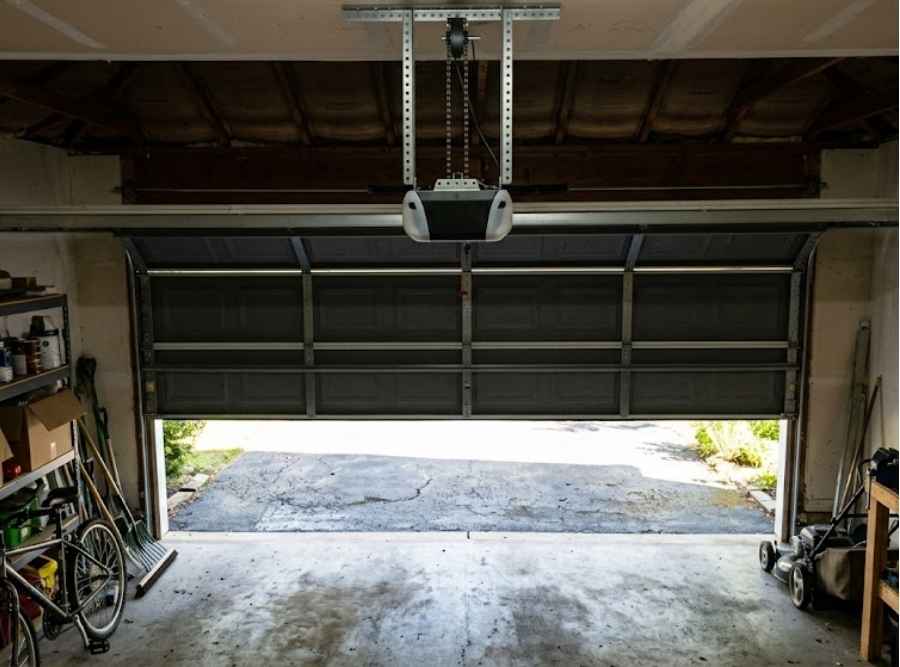 Interior view of a partially open garage door with overhead opener rail and daylight
